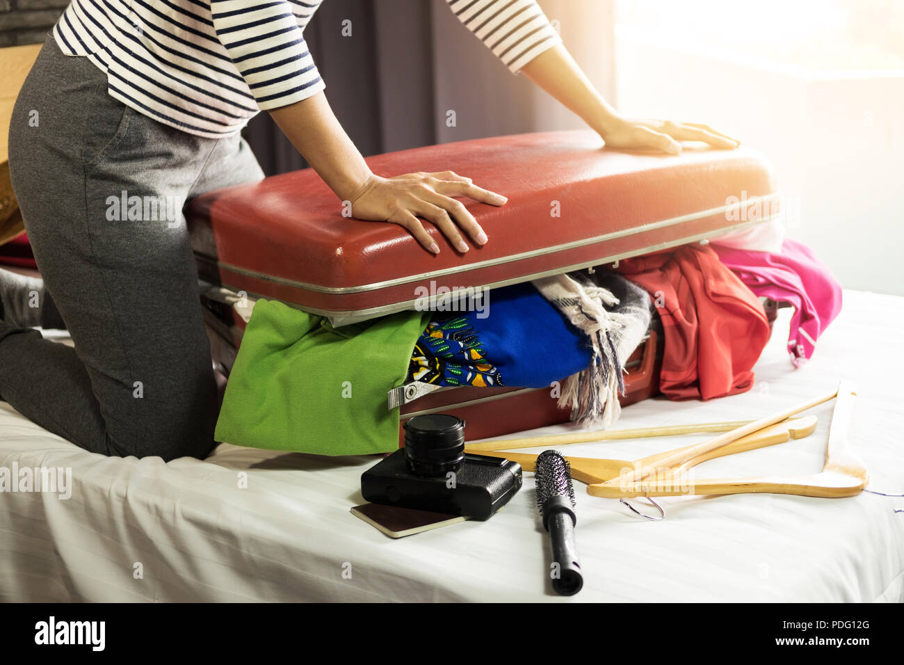 Woman trying to fit all clothing to packing her red suitcase before