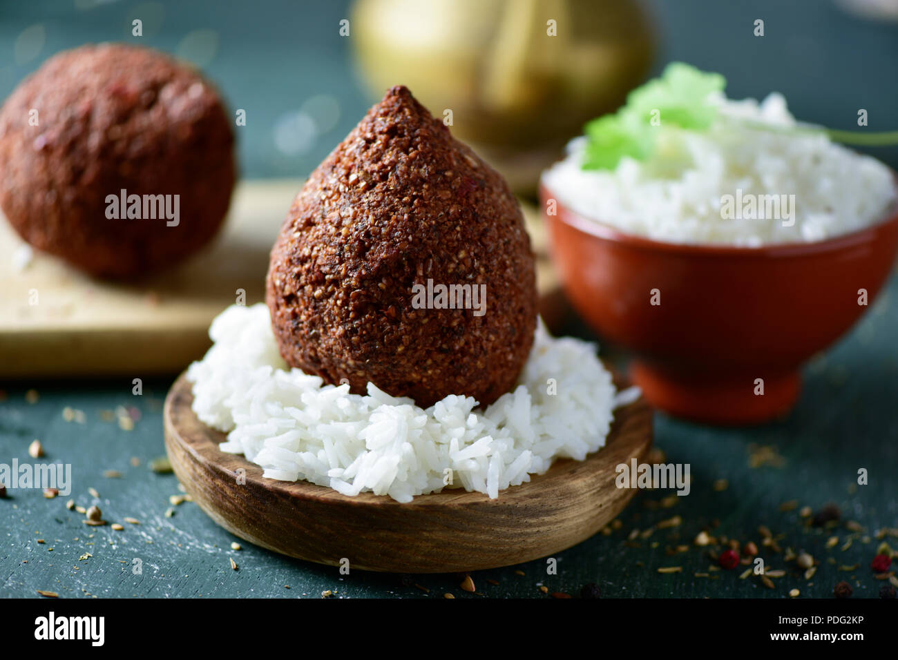 kibbeh, a levantine dish, and an earthenware bowl with rice on a rustic wooden table, with a golden teapot in the background Stock Photo