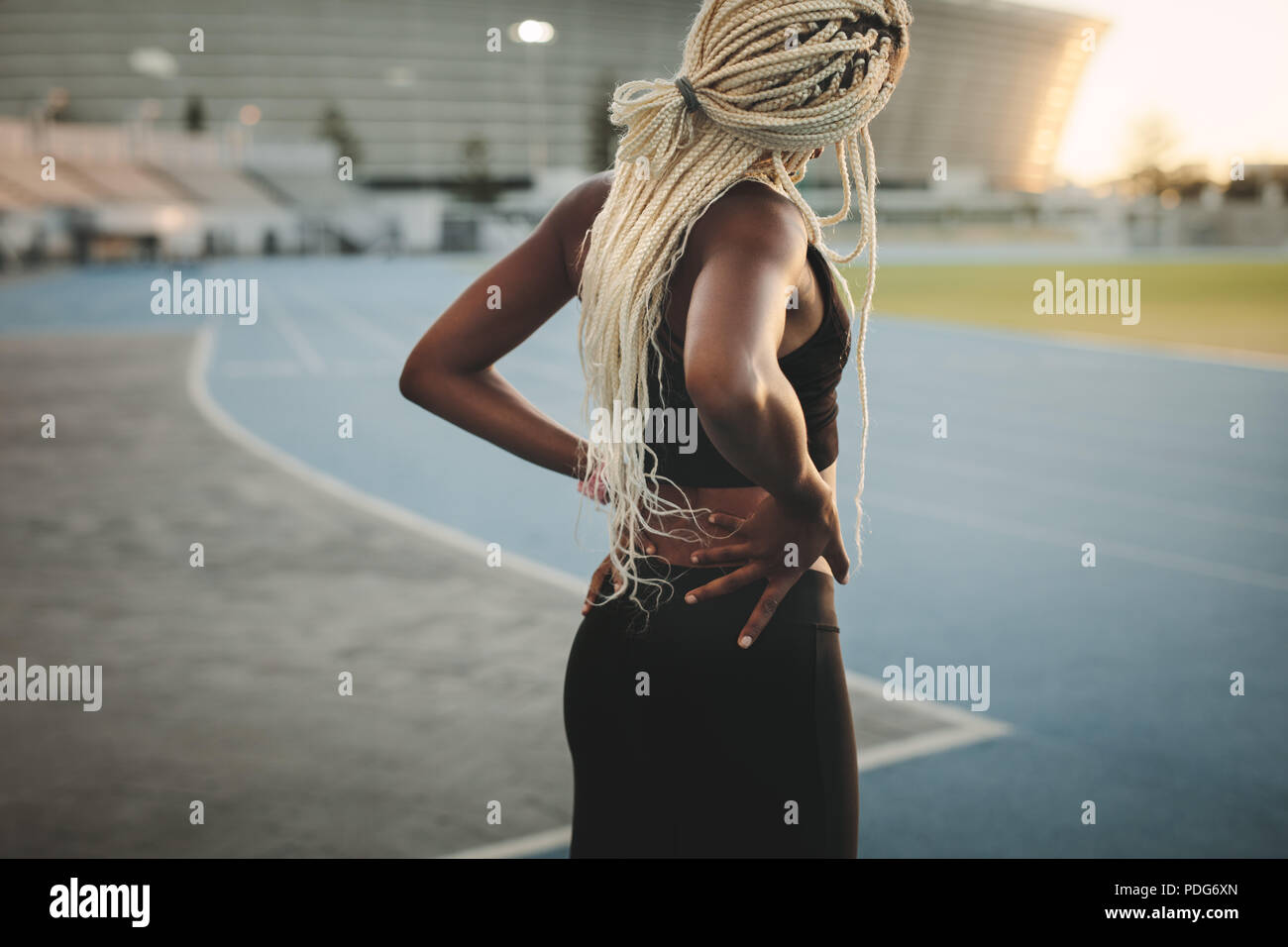 Rear view of a female runner warming up before a run with hands on hips. Woman athlete doing exercises in a track and field stadium. Stock Photo