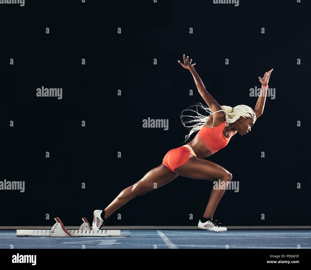 Side view of a female athlete starting her sprint on an all-weather running track on a black background. Runner using starting block to start her run Stock Photo