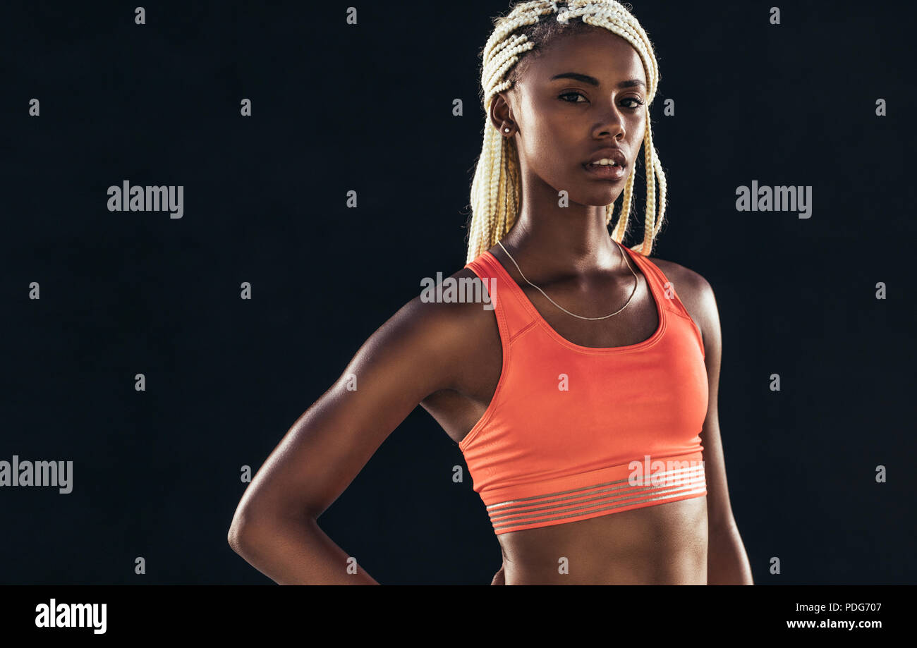 Portrait of a female athlete on a black background. Woman sprinter in fitness attire standing with hand on hip. Stock Photo