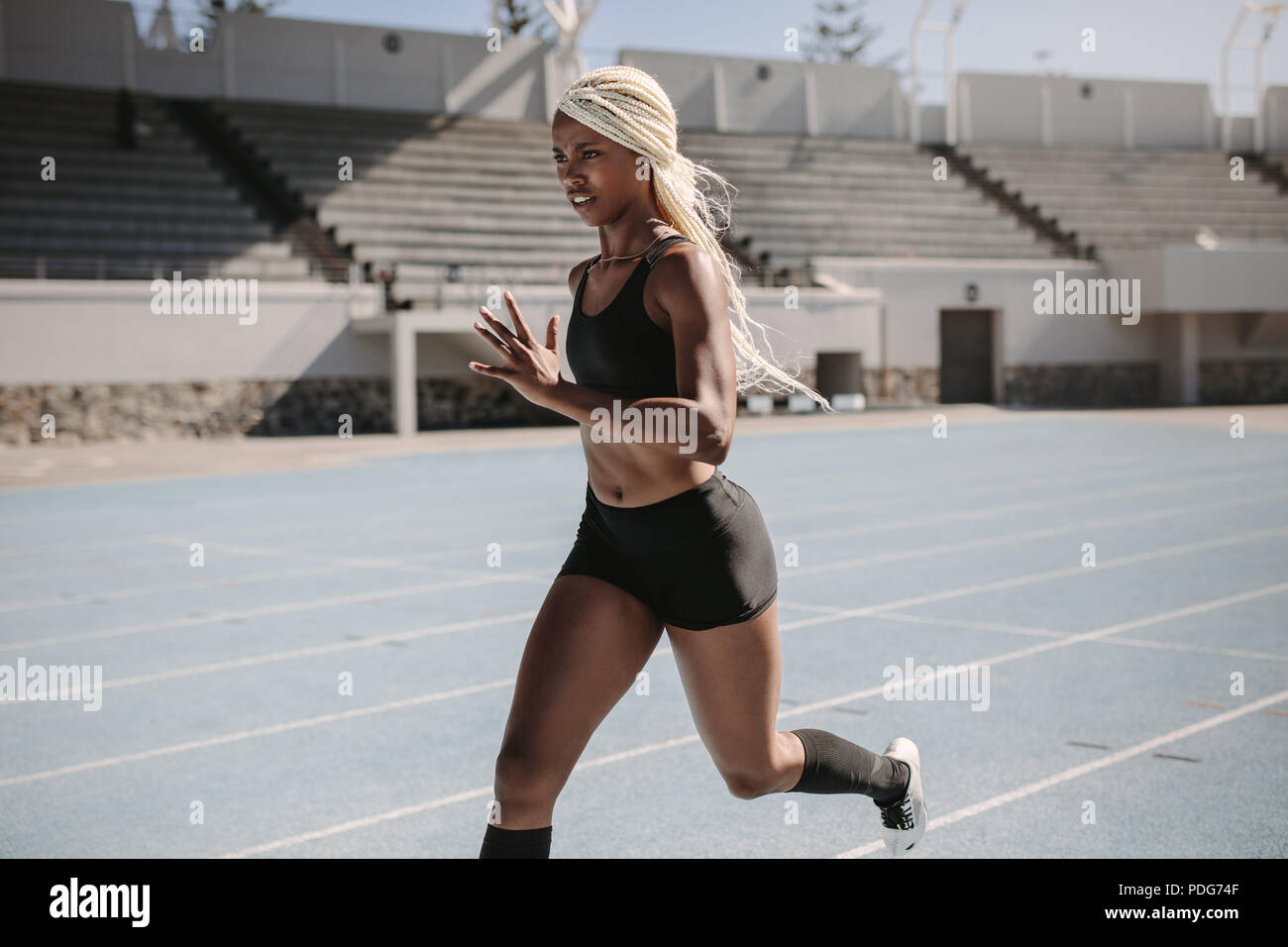 Side view of a female athlete sprinting on a running track in a track and field stadium. Female runner training on a running track. Stock Photo