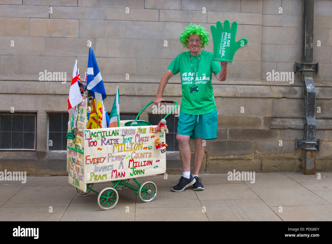 Pram man John a charity worker & collector for Macmillan Cancer support wearing a green wig and wheeling a wooden pram in Sheffield, UK. Macmillan Cancer Support is one of the largest British charities and provides specialist health care, information and financial support to people affected by cancer Stock Photo