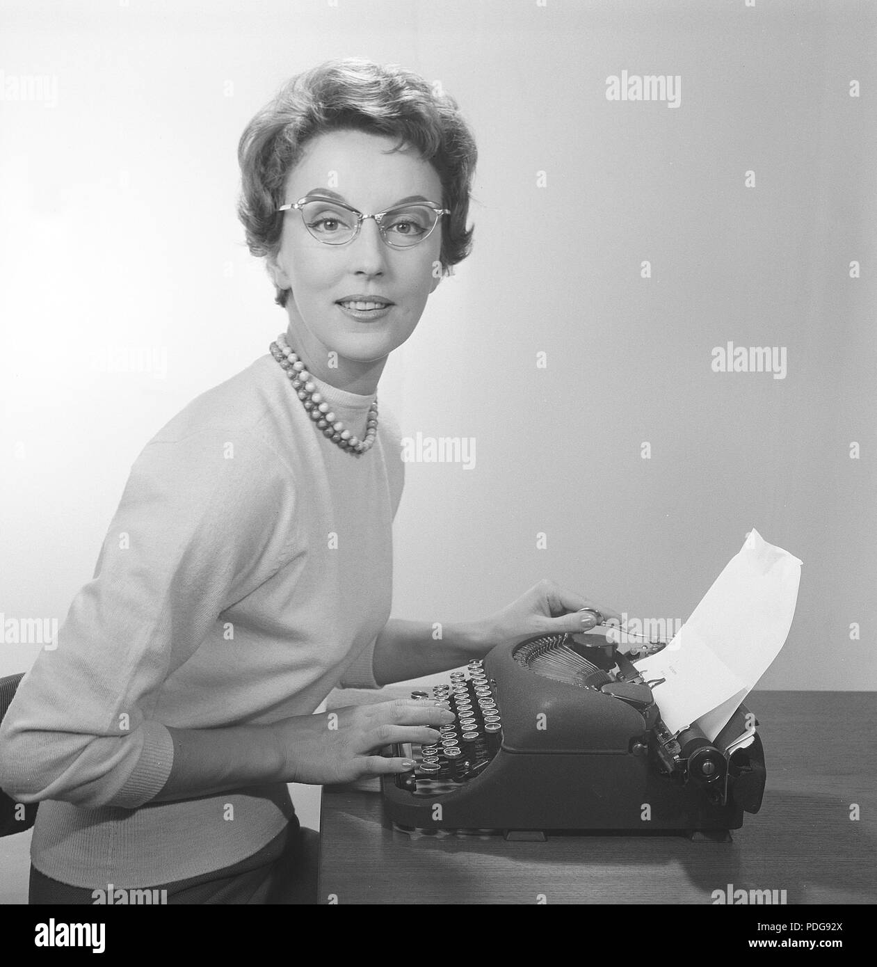 Office girl in the 1950s. A young girl at her typewriter is wearing typical fifties glasses and jumper. 1958. Photo Kristoffersson/CB96-10 Stock Photo