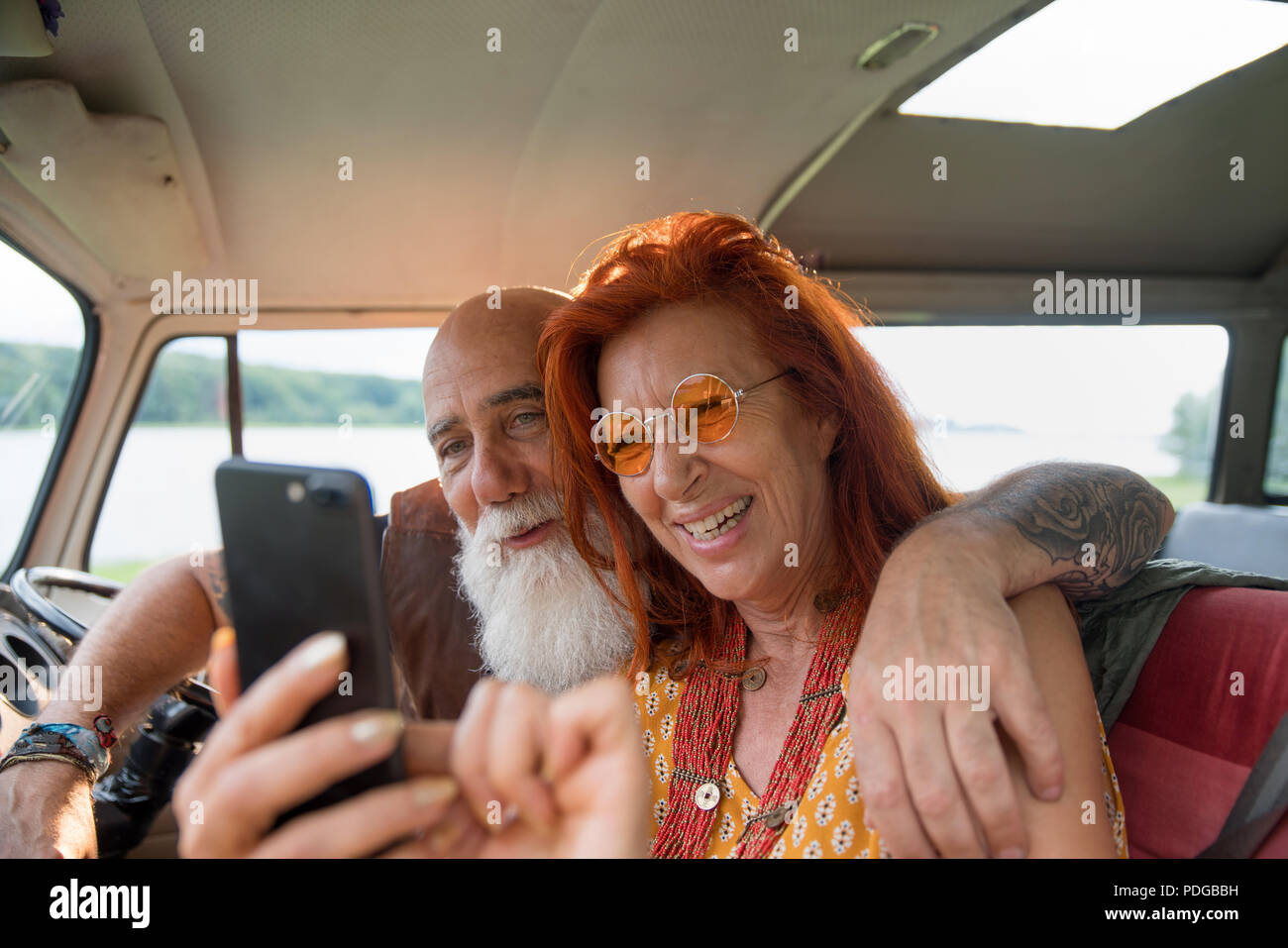 Old hipster couple using a smartphone inside their camper van  Stock Photo