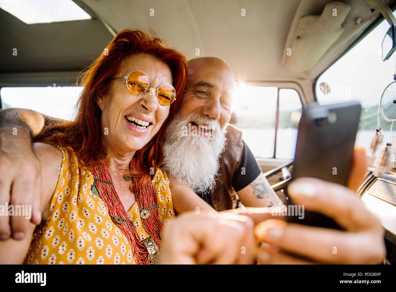 Old hipster couple using a smartphone inside their vintage van  Stock Photo