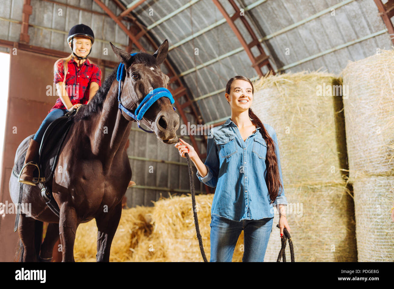 Darkhaired stylish riding teacher leading horse with cute girl Stock