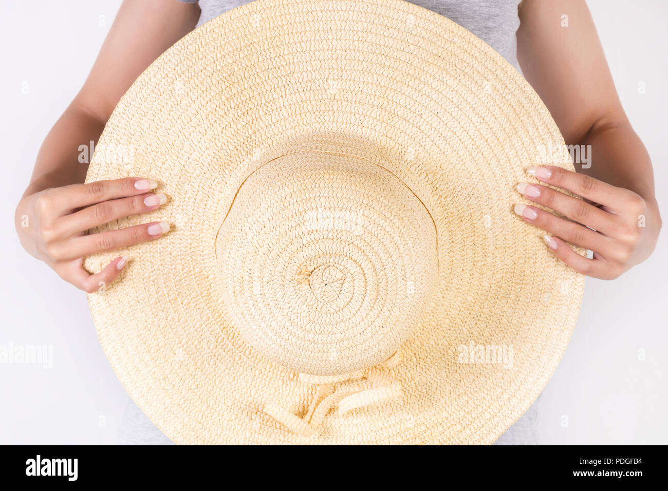 Beautiful young woman holding big straw hat in hand isolated on white background. Summer concept clothes. Close up, selective focus Stock Photo