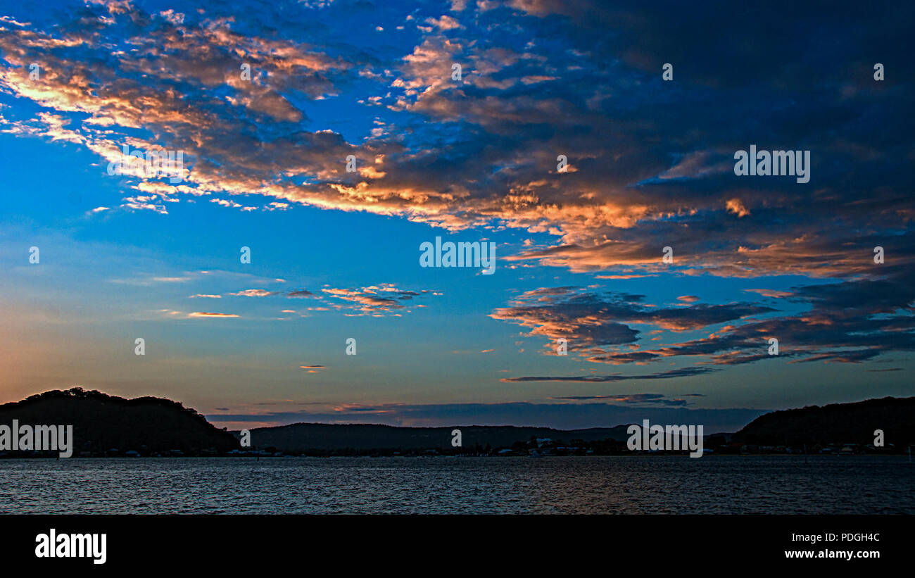 Picturesque non urban coastal orange cloud, cobalt blue sky, sunset landscape. With mostly stratocumulus clouds over water and a seashore horizon. Stock Photo