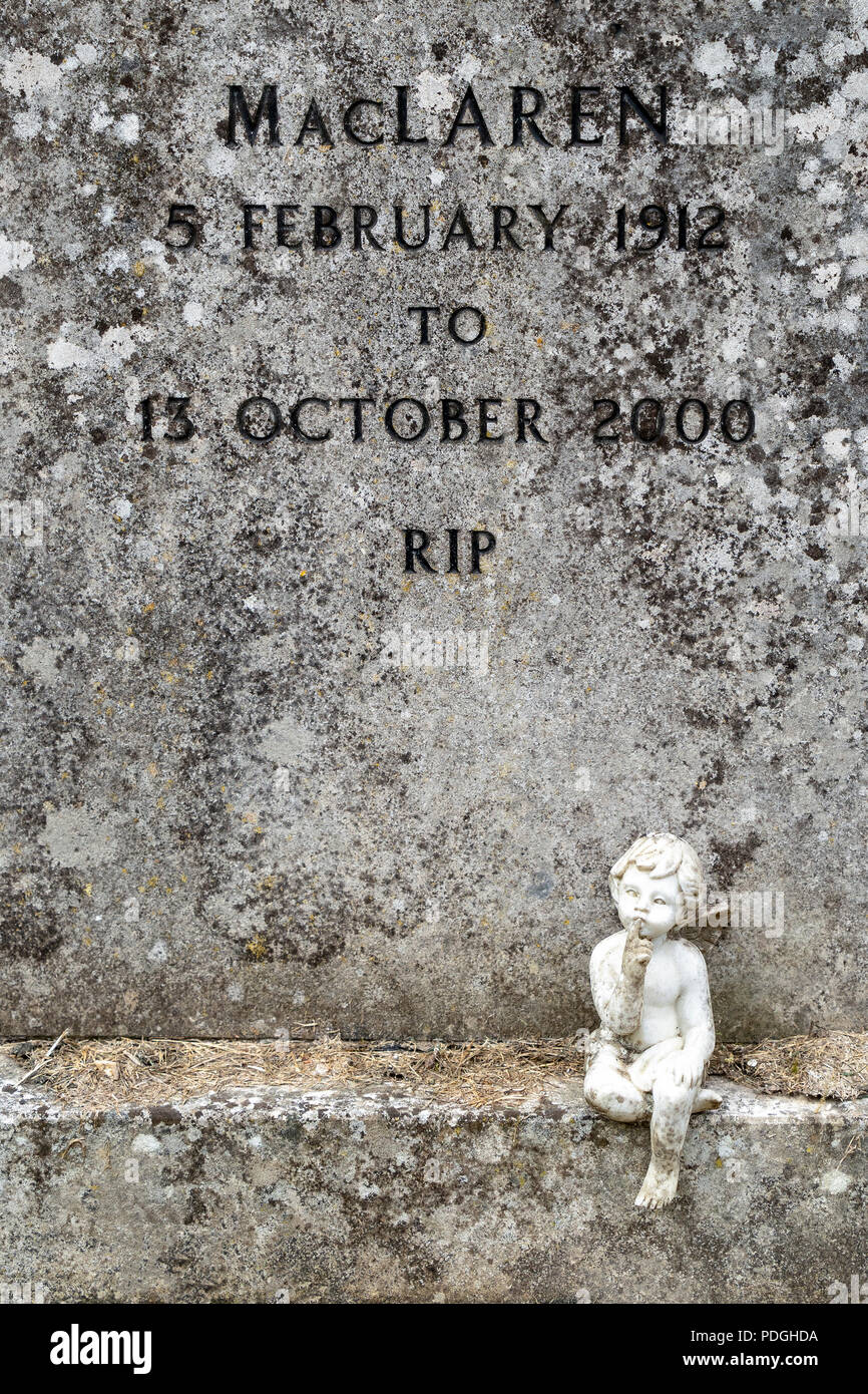 Small statue sitting at the base of grave stone Stock Photo