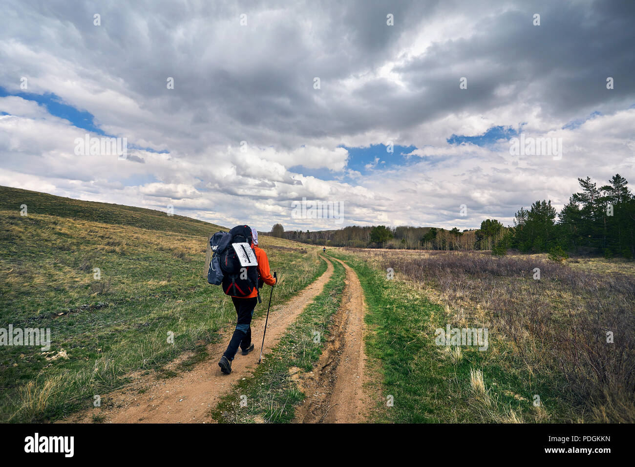 Hiker in with big backpack walking to the country road near the forest against cloudy sky in Karkaraly national park in Central Kazakhstan Stock Photo