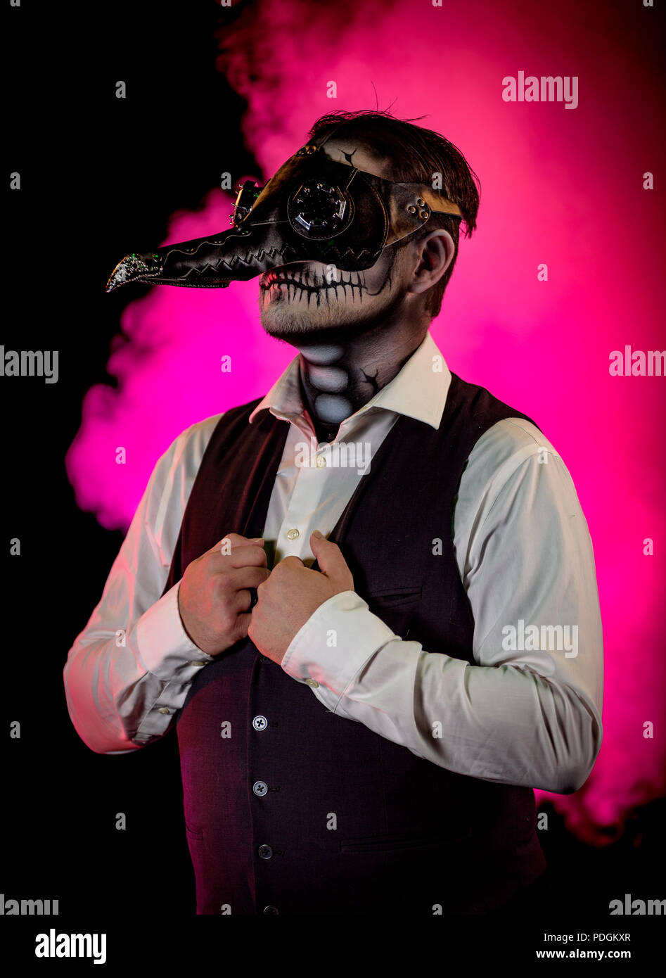 Portrait of a nicely dressed man wearing a plague doctor mask and skull makeup. Horror and Halloween themed, shot with theatrical lighting and effects Stock Photo