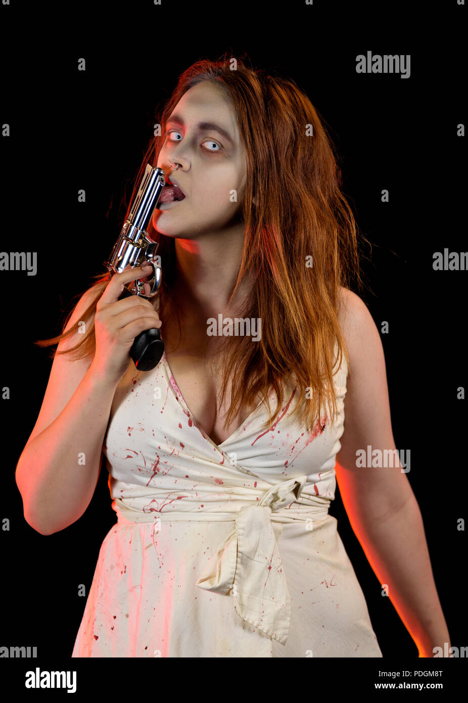 A caucasian female model as an undead character holding a revolver pistol. Model is wearing a white dress and has custom theatrical makeup. Shot again Stock Photo