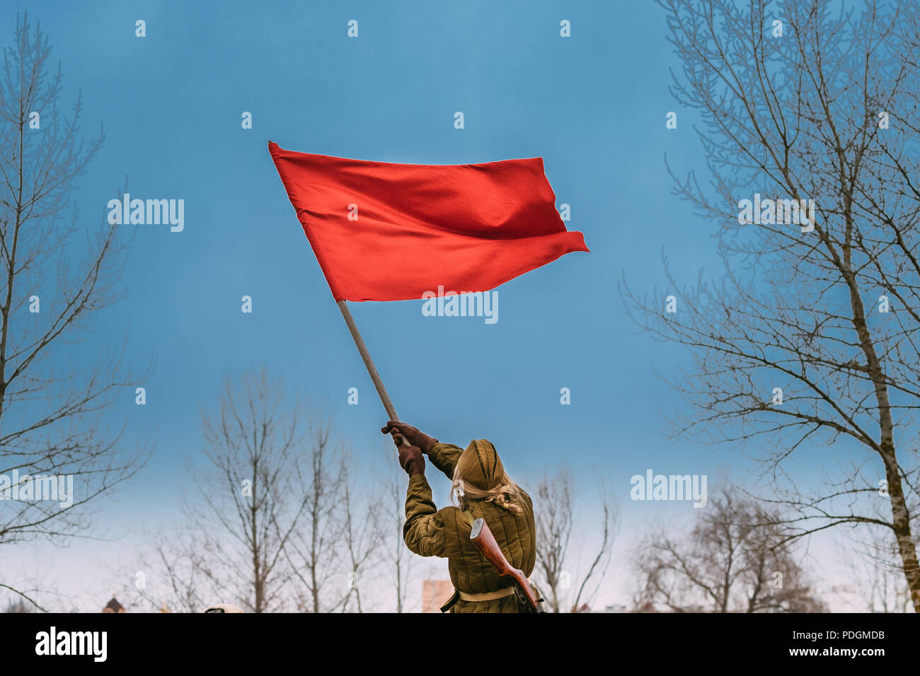 Gomel, Belarus - November 26, 2016: Young Woman Re-enactor Dressed As Russian Soviet Red Army Soldier Of World War II Waving A Red Flag In Honor Of Vi Stock Photo
