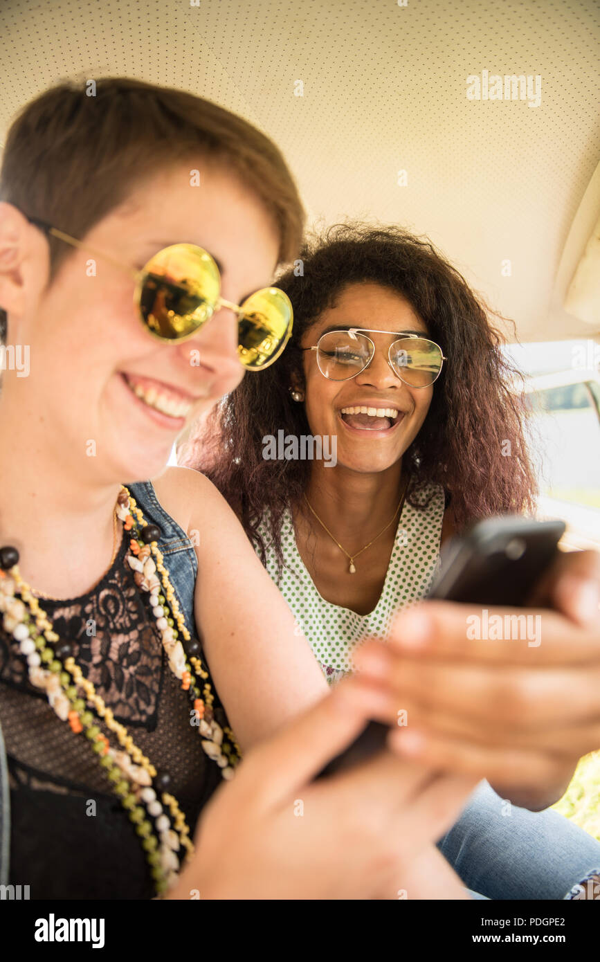 Two young mixed women having fun using a smartphone. Stock Photo