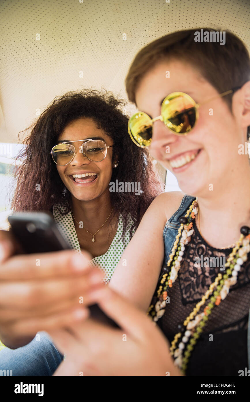 Two young mixed women having fun using a smartphone. Stock Photo
