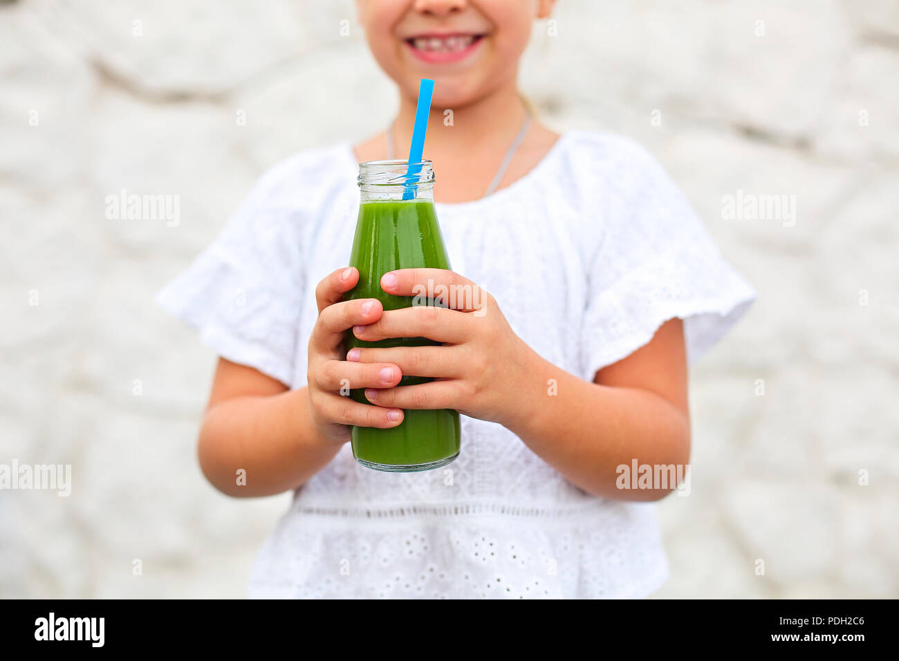 Little girl is drinking green fresh juice using straw outdoors. Close up Stock Photo