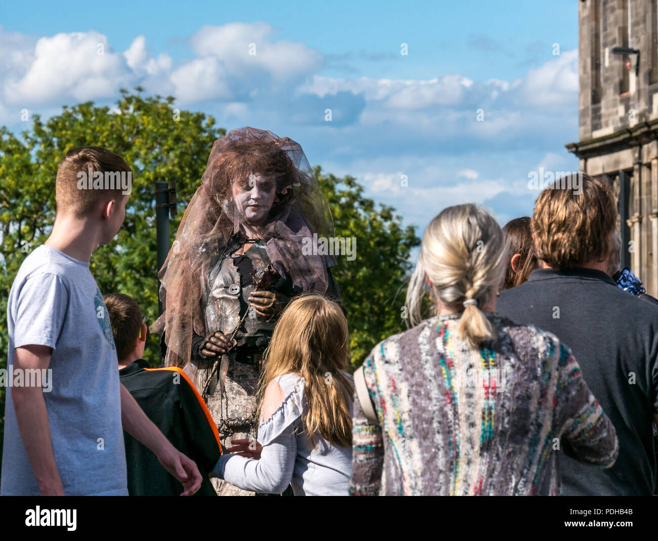 Edinburgh, Scotland, UK. 9th August 2018. Edinburgh Fringe Festival, Royal Mile, Edinburgh, Scotland, United Kingdom. On a sunny festival day the Virgin Money sponsored street festival is packed with people and fringe performers. A female street performer dressed as a ghostly woman stands above the pedestrians Stock Photo