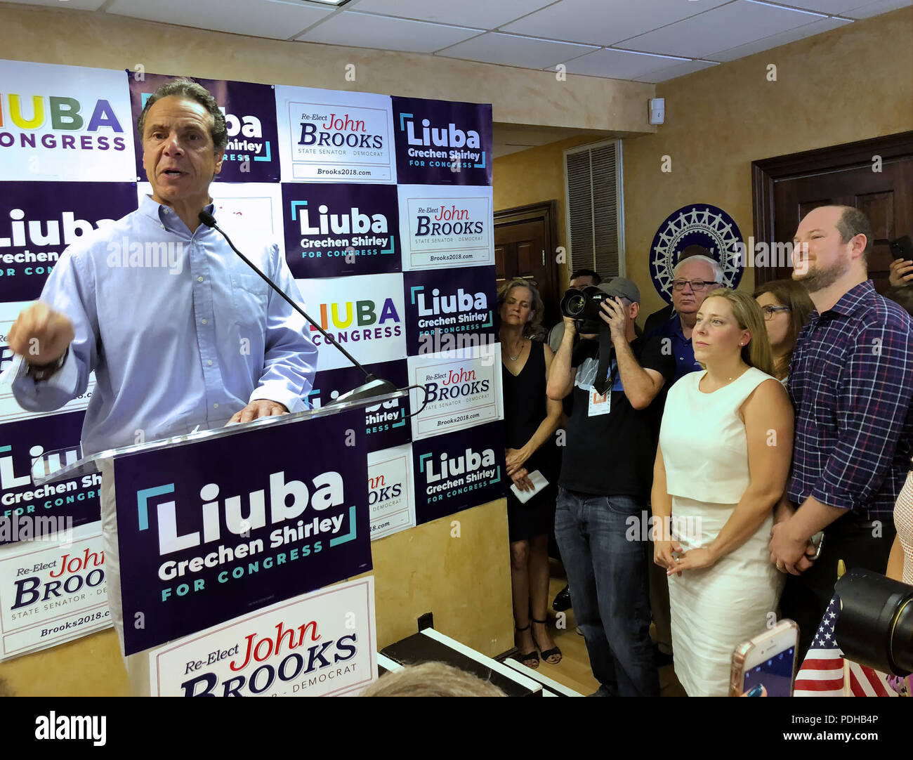 Massapequa, New York, USA. 5th Aug, 2018. Governor ANDREW CUOMO speaks at podium, as (by cirucular wall sign) NY Senator JOHN BROOKS; LIUBA GRECHEN SHIRLEY, Congressional candidate for NY 2nd District; and her husband CHRIS SHIRLEY, at extreme right; and others listen at opening of joint campaign office, aiming for a Democratic Blue Wave in November midterm elections. Credit: Ann Parry/ZUMA Wire/Alamy Live News Stock Photo
