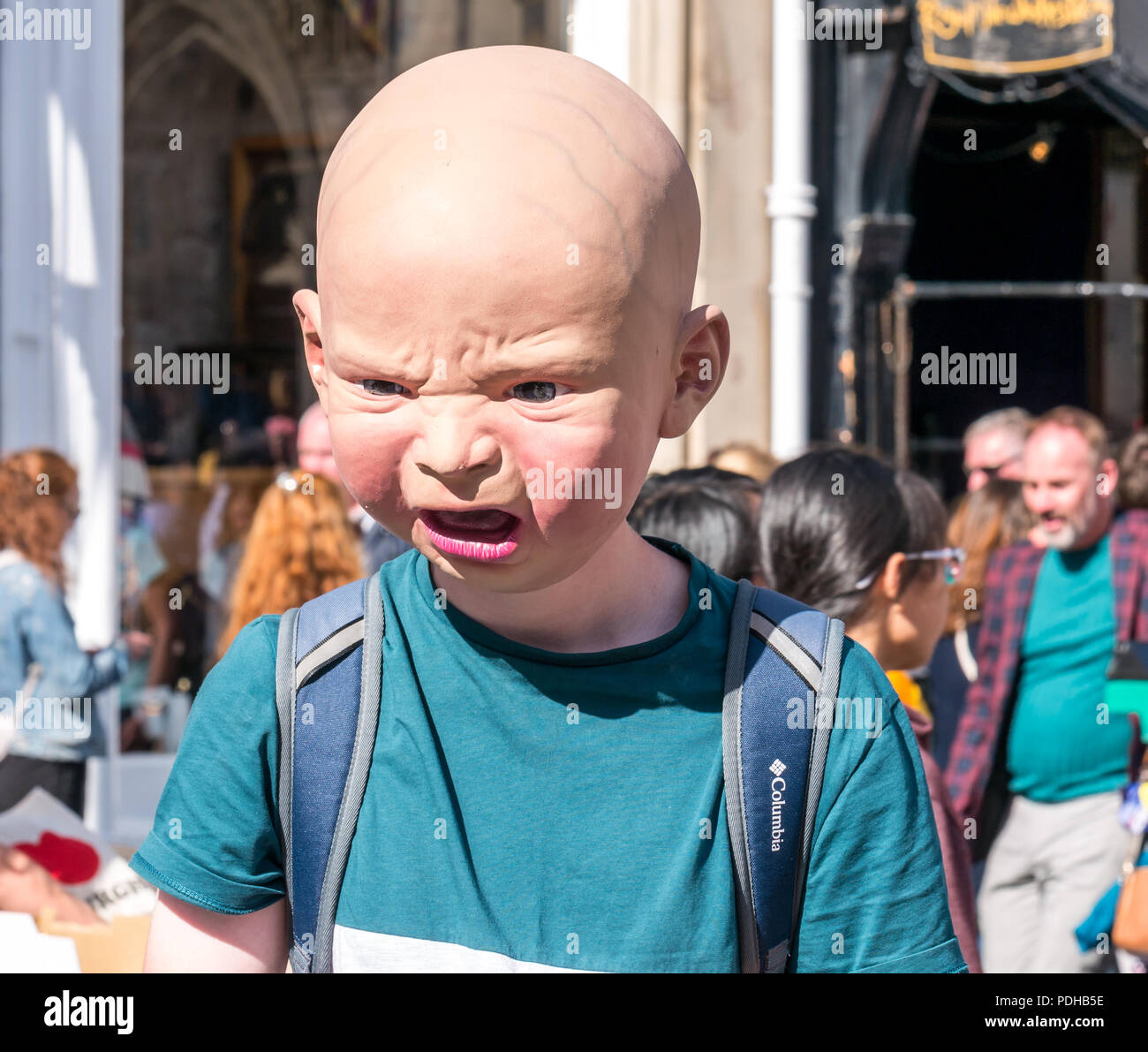 Edinburgh, Scotland, UK. 9th August 2018. Edinburgh Fringe Festival, Royal Mile, Edinburgh, Scotland, United Kingdom. On a sunny festival day the Virgin Money sponsored street festival is packed with people and fringe performers. A Fringe performer wearing a gruesome baby head interacts with pedestrians handing out flyers Stock Photo