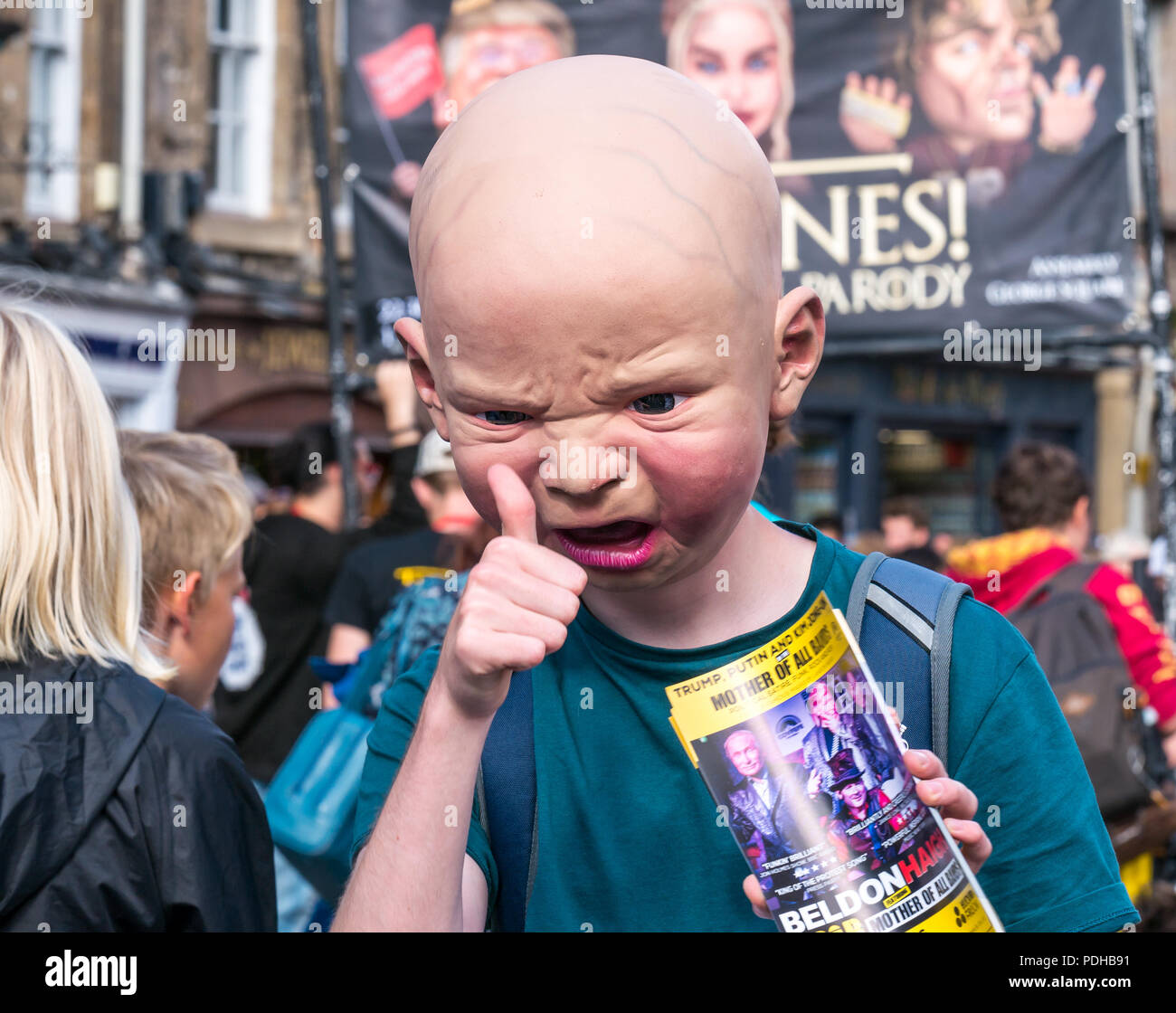 Edinburgh, Scotland, UK. 9th August 2018. Edinburgh Fringe Festival, Royal Mile, Edinburgh, Scotland, United Kingdom. On a sunny festival day the Virgin Money sponsored street festival is packed with people and fringe performers. A Fringe performer wearing a gruesome baby head interacts with pedestrians and hands out flyers Stock Photo