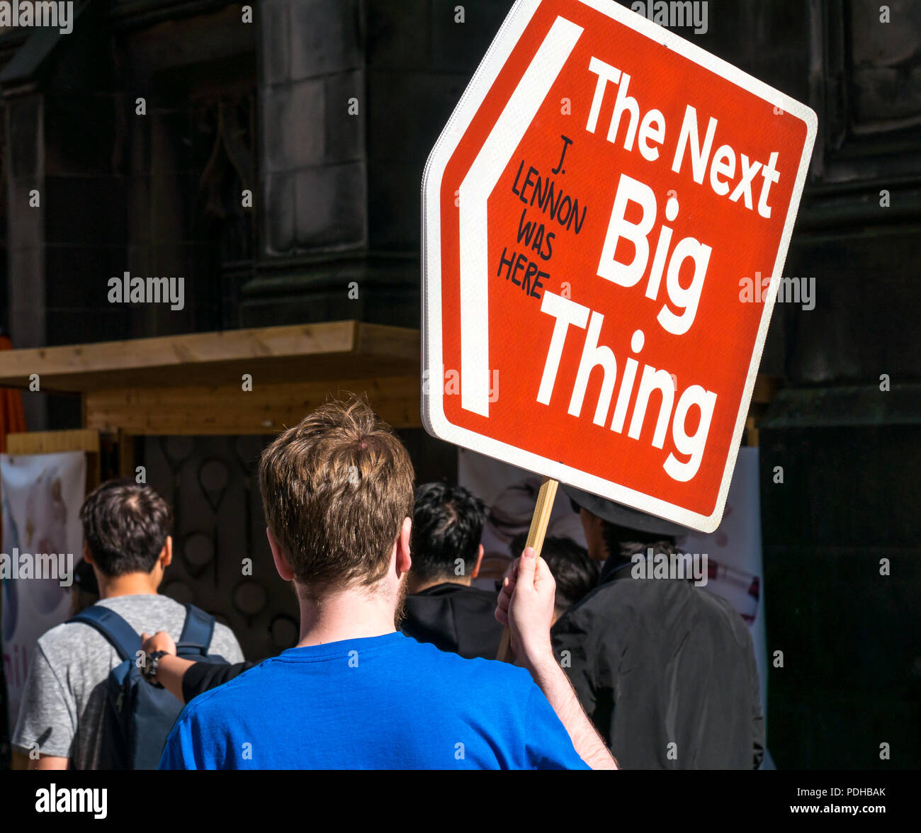 Edinburgh, Scotland, UK. 9th August 2018. Edinburgh Fringe Festival, Royal Mile, Edinburgh, Scotland, United Kingdom. On a sunny festival day the Virgin Money sponsored street festival is packed with people and fringe performers. A man holding an arrow sign saying The Next Big Thing Stock Photo
