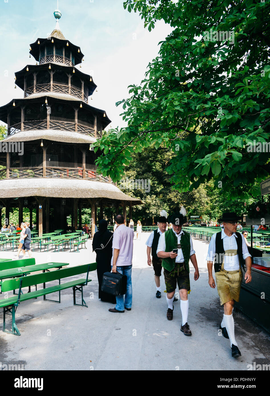 Munich, Germany - July 29, 2018: Traditionally dressed Bavarian men next to the Chinese Tower in English gardens . Muslim woman in full black veil Stock Photo