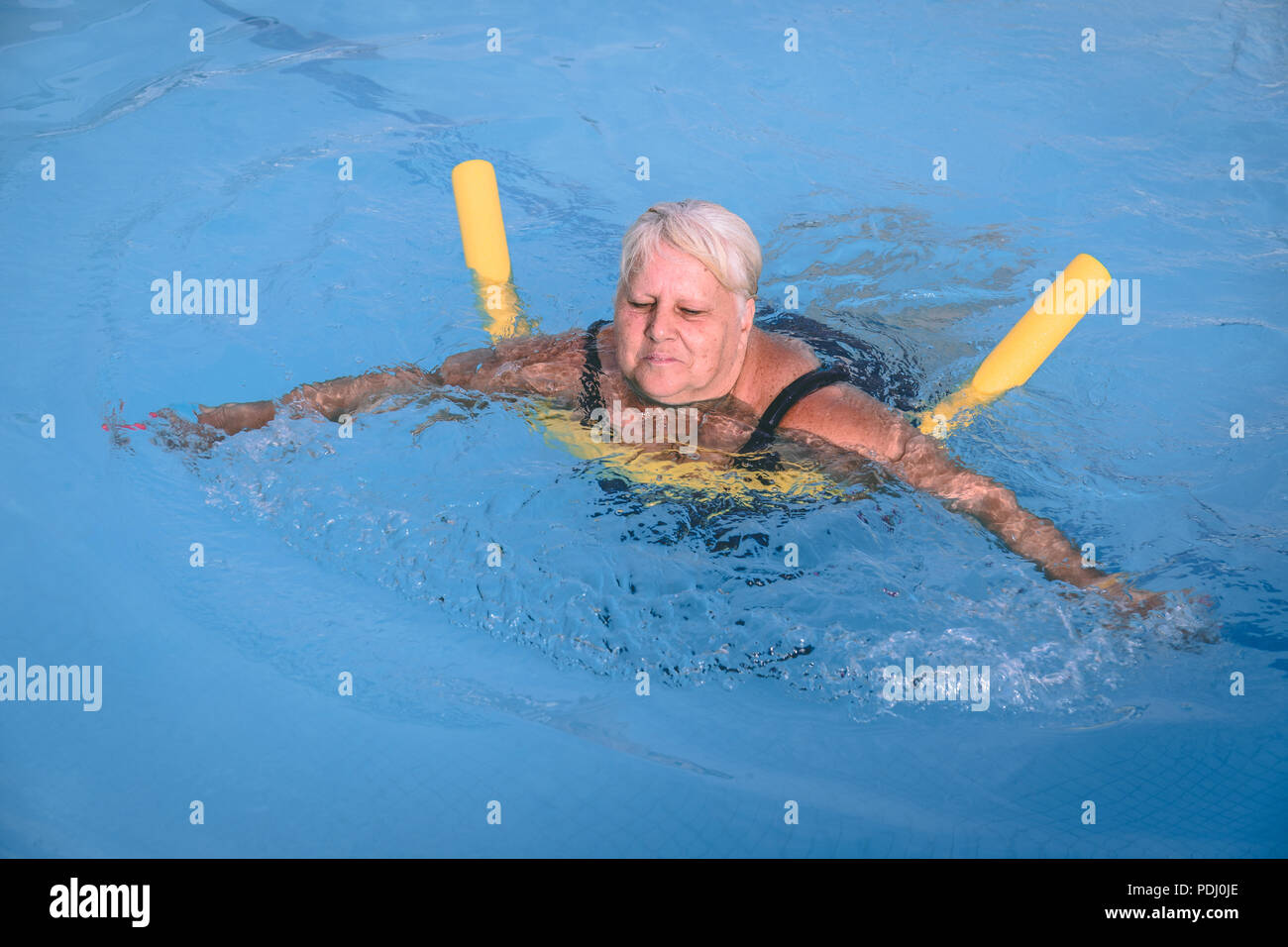 A senior female woman holds on to a flotation device on a swimming pool