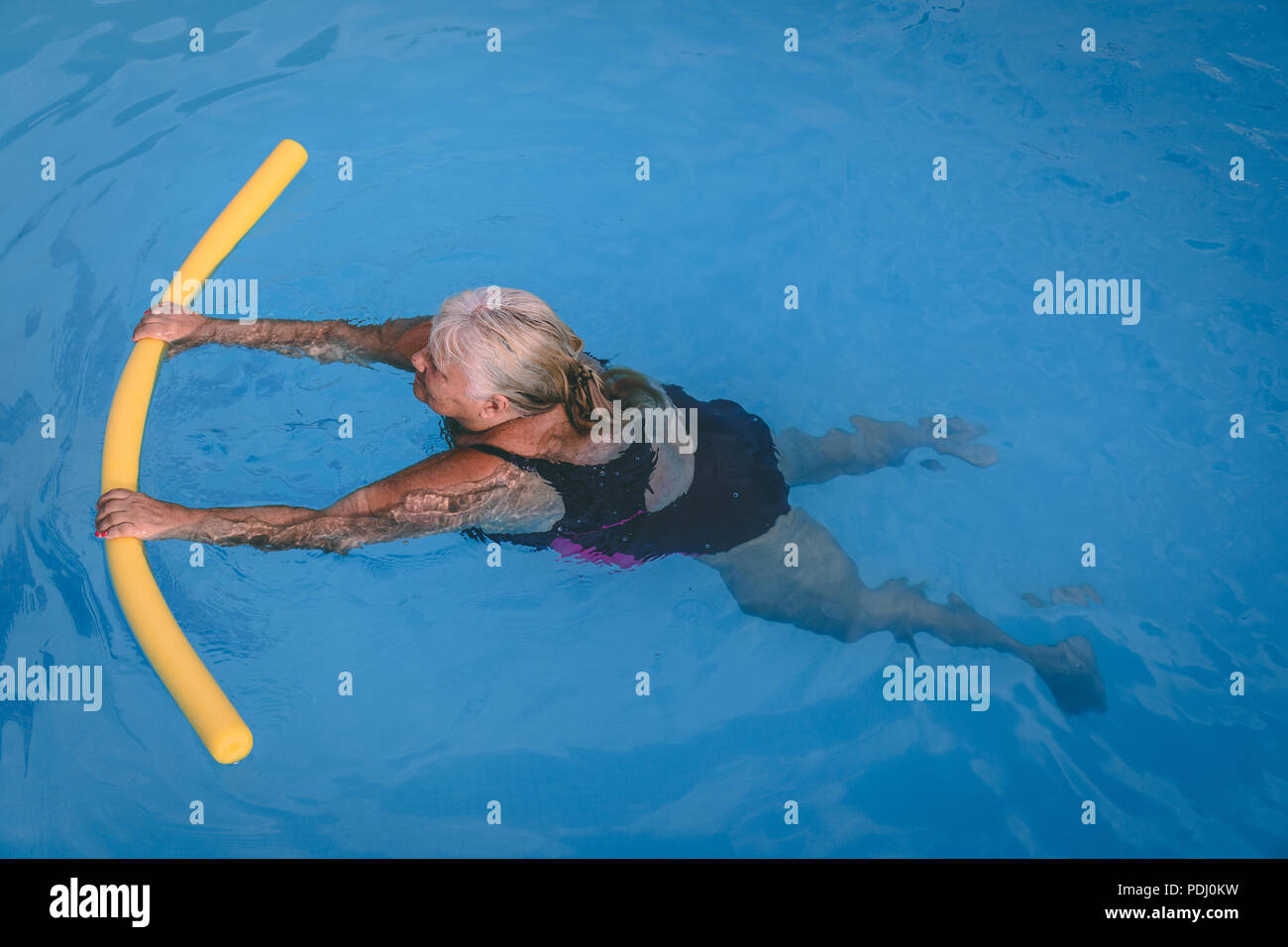 A senior female woman holds on to a flotation device on a swimming pool