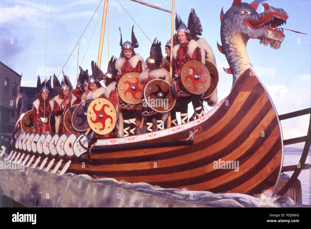 1960s people dressed up in Viking costumes, with helmets and shields, standing on a reconstrution of Viking sea transport, a longship, a long rowing boat. The vikings were Norse seafarers who invaded and raided Britain between the 8th-11th centuries and had a reputation as fierce warriors. Stock Photo