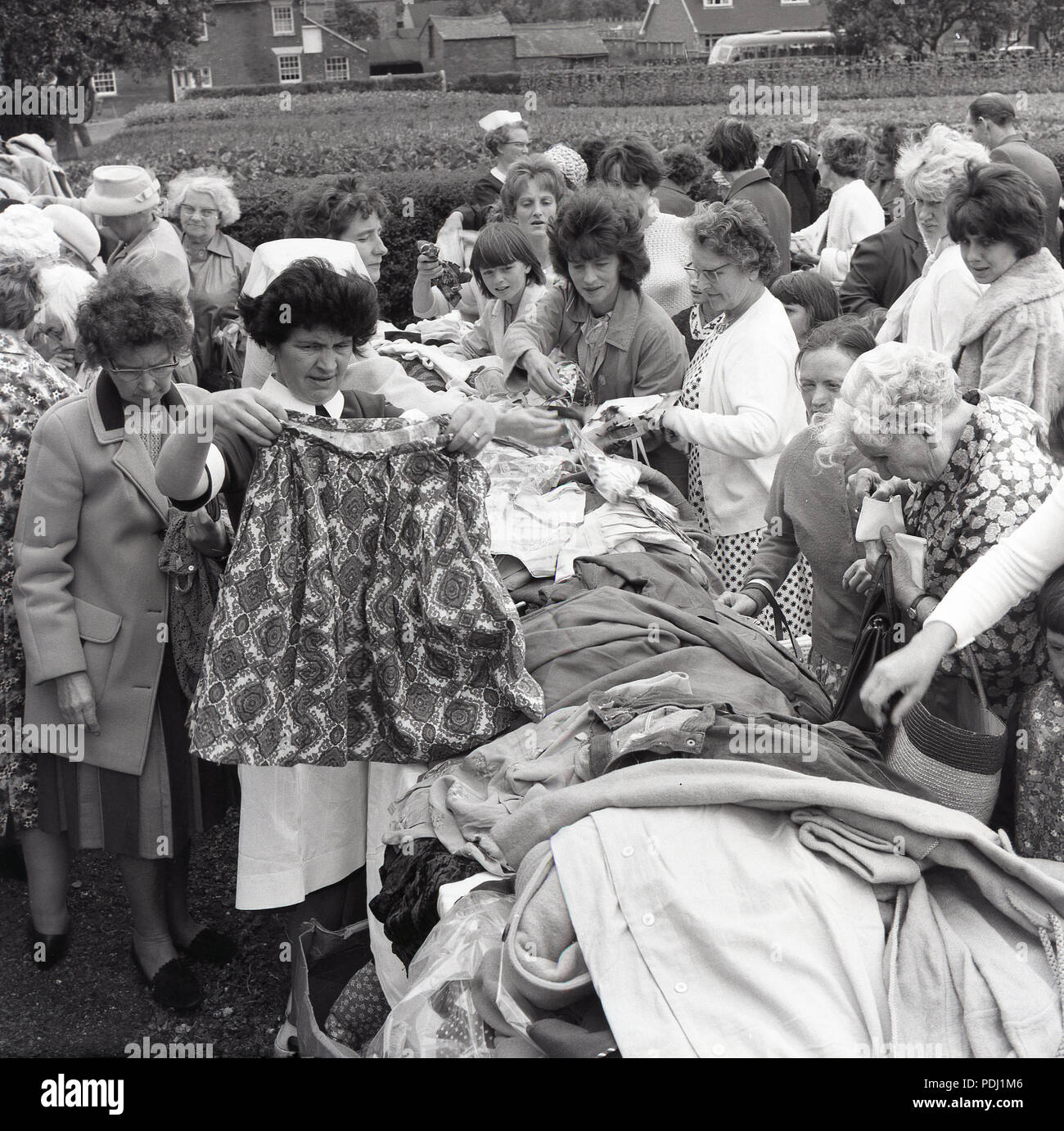 1960s, women eagerly rummaging through a large pile of second-hand clothing and soft furnishings on an outside stall at a village charity fete, England, UK. Stock Photo