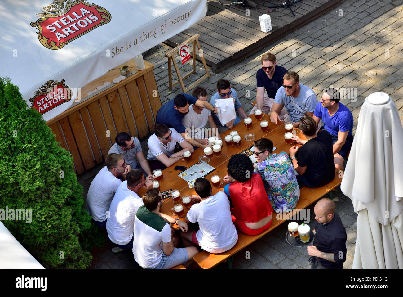 Group of men sitting around an outside bar table with glasses of beer and more beer being delivered, Prague, Czech Republic Stock Photo