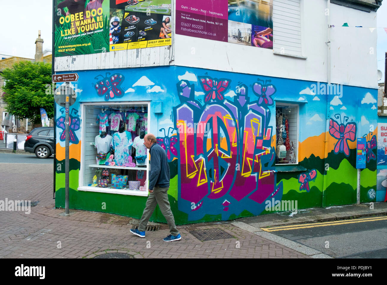 A man walking past a shop store with colourful graffiti covered walls in Newquay Cornwall. Stock Photo