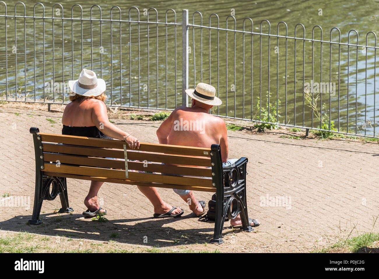 Mature holidaymakers sitting on a bench sunbathing in Trenance Park in Newquay Cornwall. Stock Photo