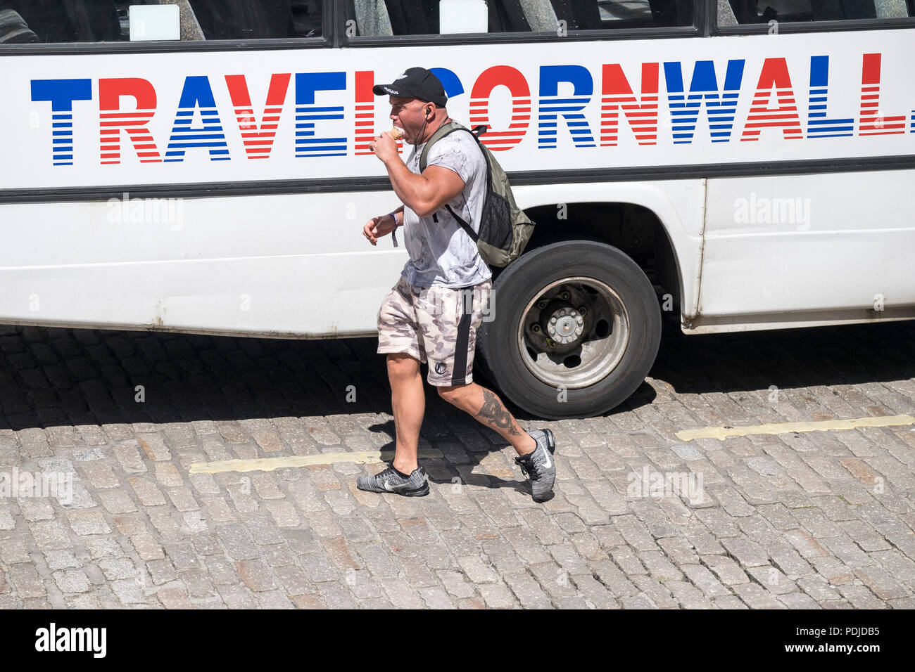 A man walking past a bus eating an ice cream in Truro Cown centre in Cornwall. Stock Photo