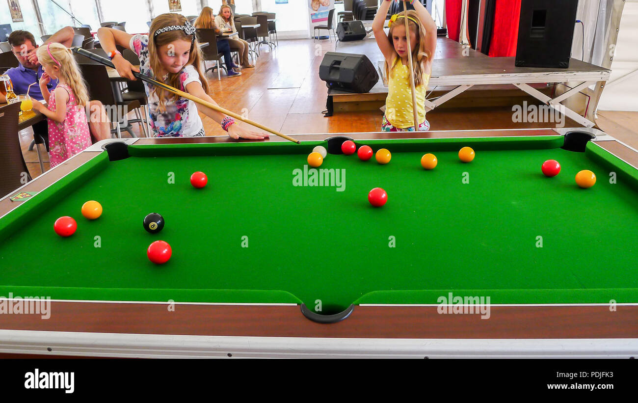 Kids, children playing pool snooker billiards holding snooker cues at snooker table Stock Photo