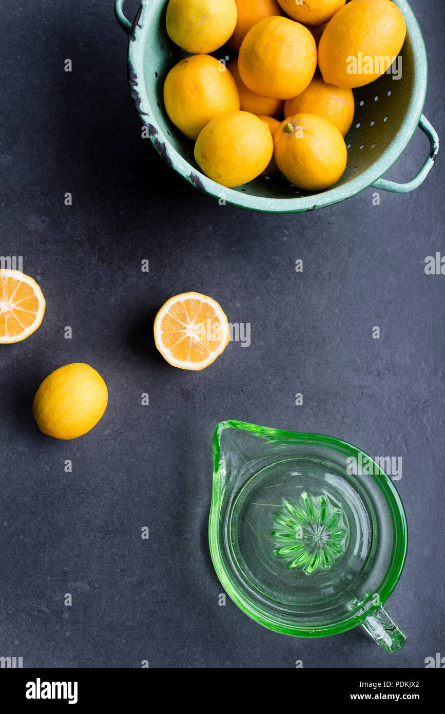 Whole and cut home grown lemons with vintage green glass juicer and colander on dark background, top view Stock Photo