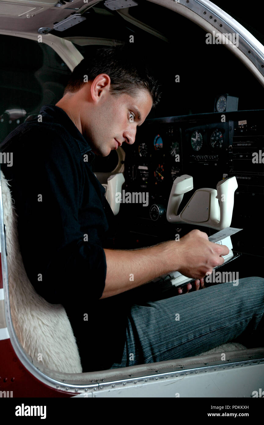 Handsome pilot reading the flight manual in the cockpit of a small