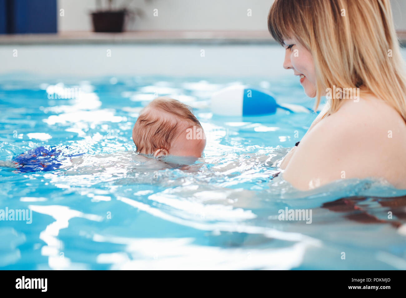 White Caucasian mother traning her newborn baby to float in swimming