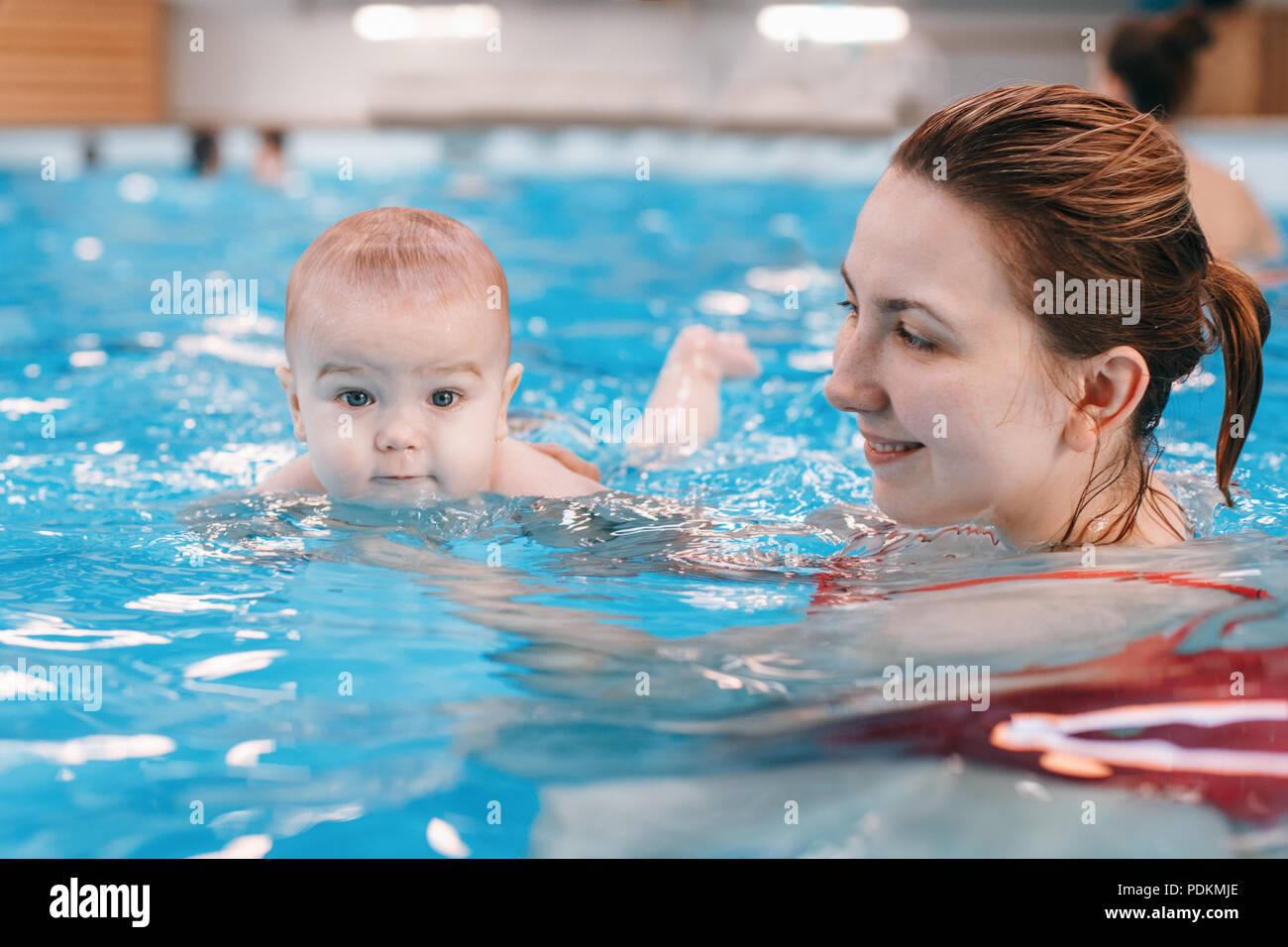 White Caucasian mother traning her newborn baby to float in swimming