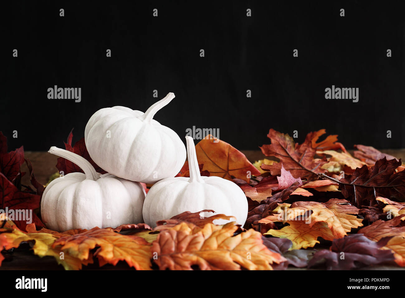 Fall leaves scattered around a stack of three white pumpkins. Extreme shallow depth of field with selective focus on pumkins. Free space for text. Stock Photo