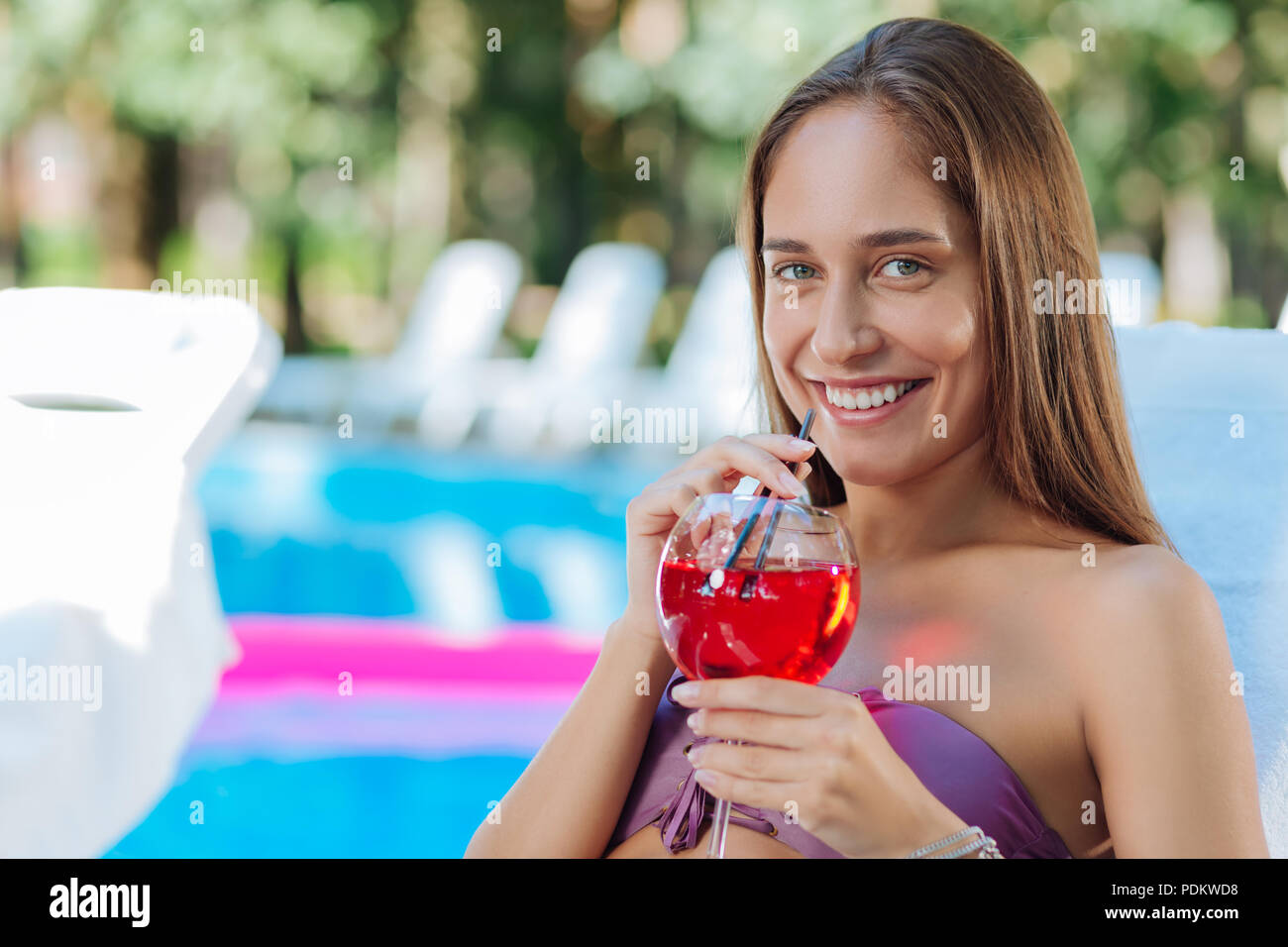 Dark-haired woman laughing while drinking summer cocktail Stock Photo