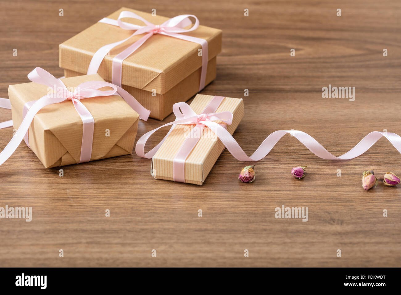 Presents concept. Close up of beige craft gift boxes with pink silky ribbon on a wooden background, copy space. Stock Photo
