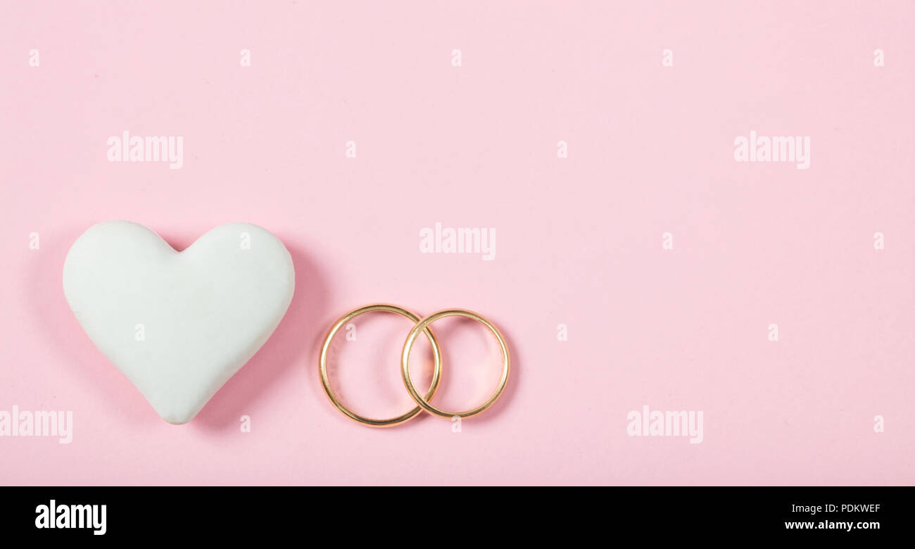 Love and marriage concept. Close up and top view of golden wedding rings and a white heart, isolated, copy space, on a pink background. Stock Photo