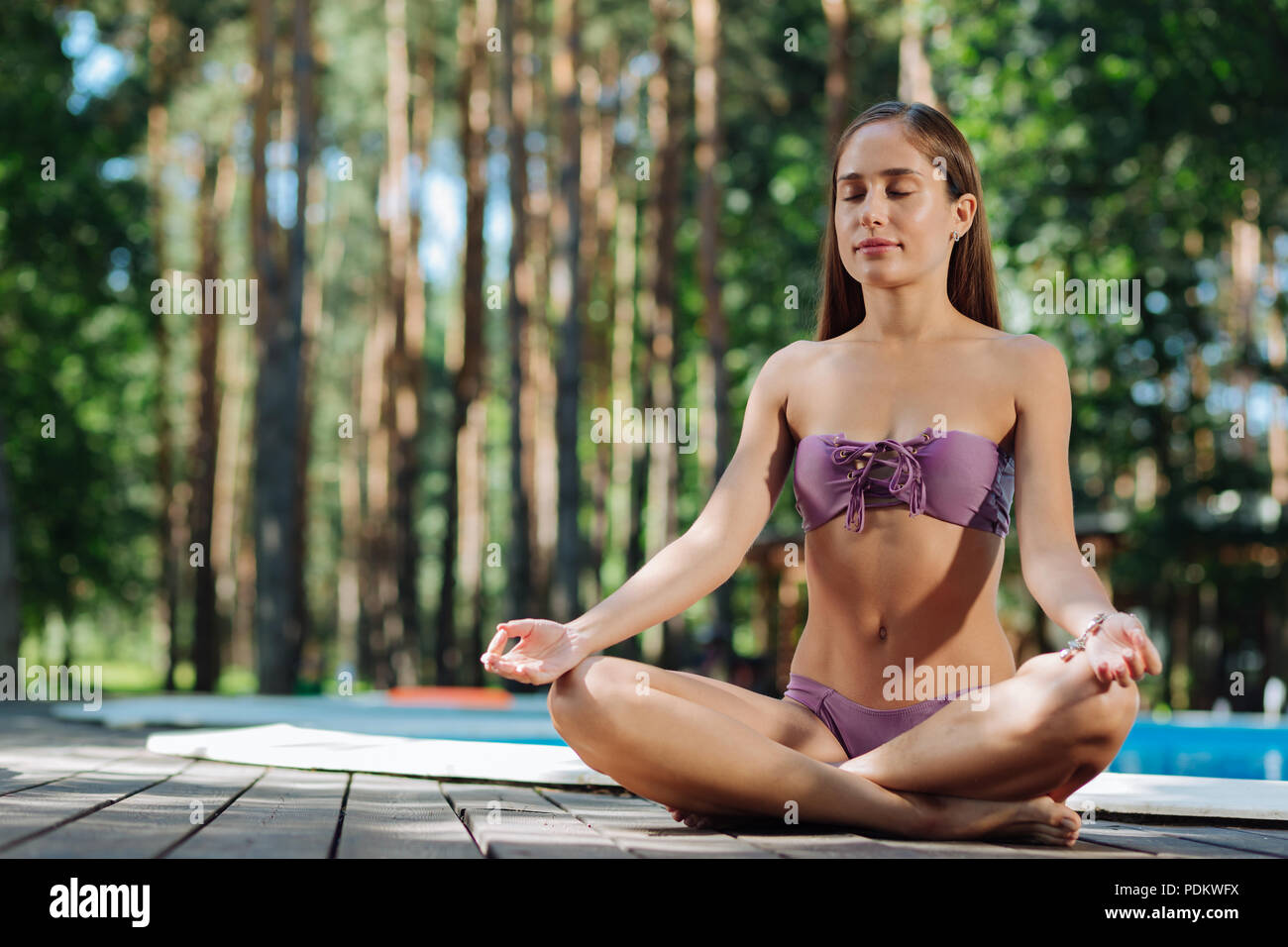 Dark-haired woman doing yoga outdoors near pool Stock Photo