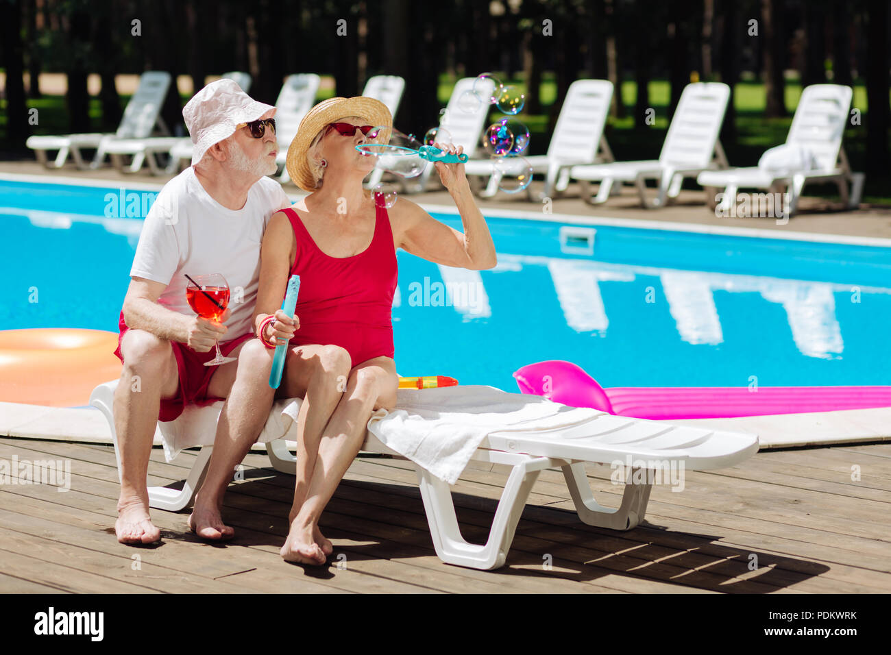 Couple of cute pensioners blowing soap bubbles near the pool Stock Photo