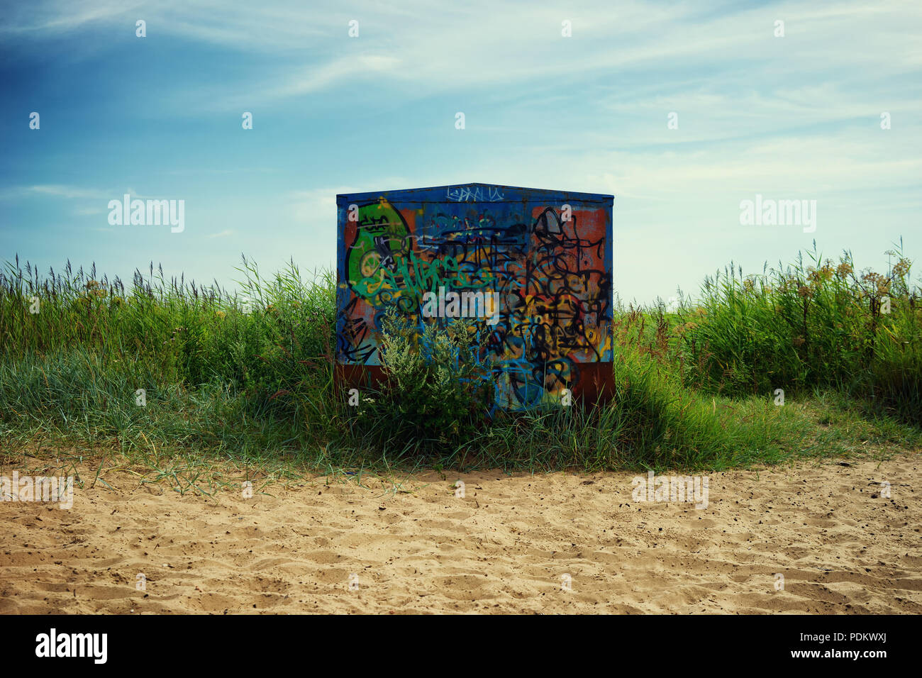 Graffiti on metal hangar on a background of blue sky on the beach in the green grass Stock Photo