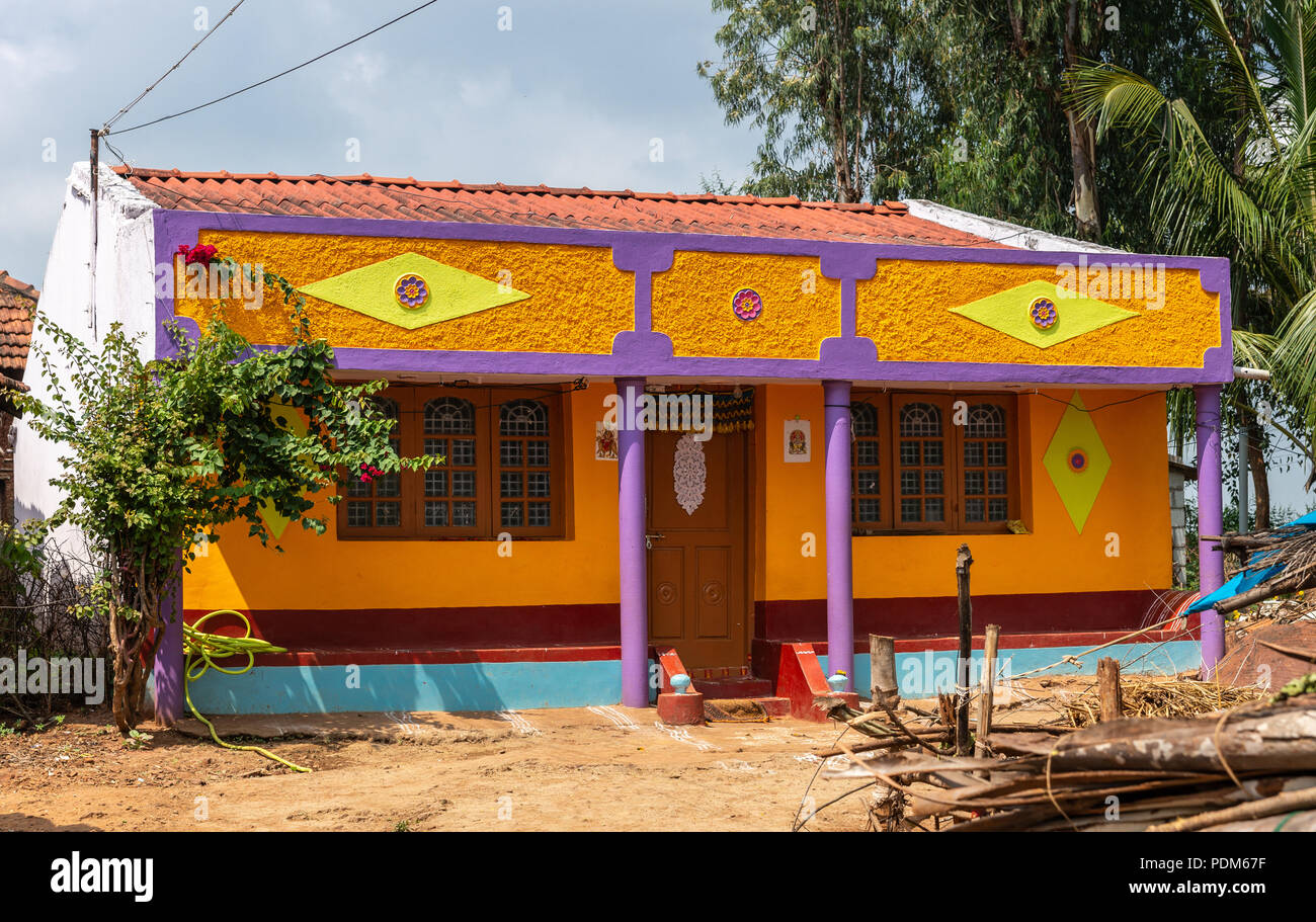 Nilavagilukaval, Karnataka, India - November 1, 2013: Brightly orange, yellow and purple painted newly built house stands in brown dirt under light bl Stock Photo