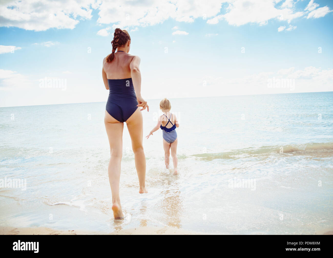 Seen From Behind Young Mother And Child In Swimwear On The Seacoast Going Into The Sea Stock Photo Alamy
