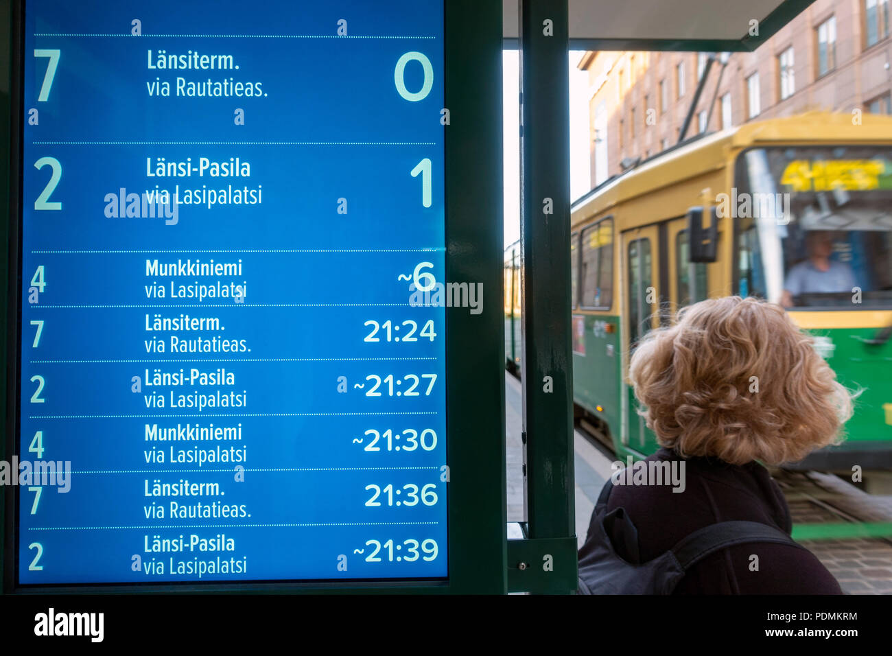 Electronic timetable display showing estimated arrival times of trams with tram arriving at tram stop on Aleksanterinkatu Street in Helsinki Finland Stock Photo